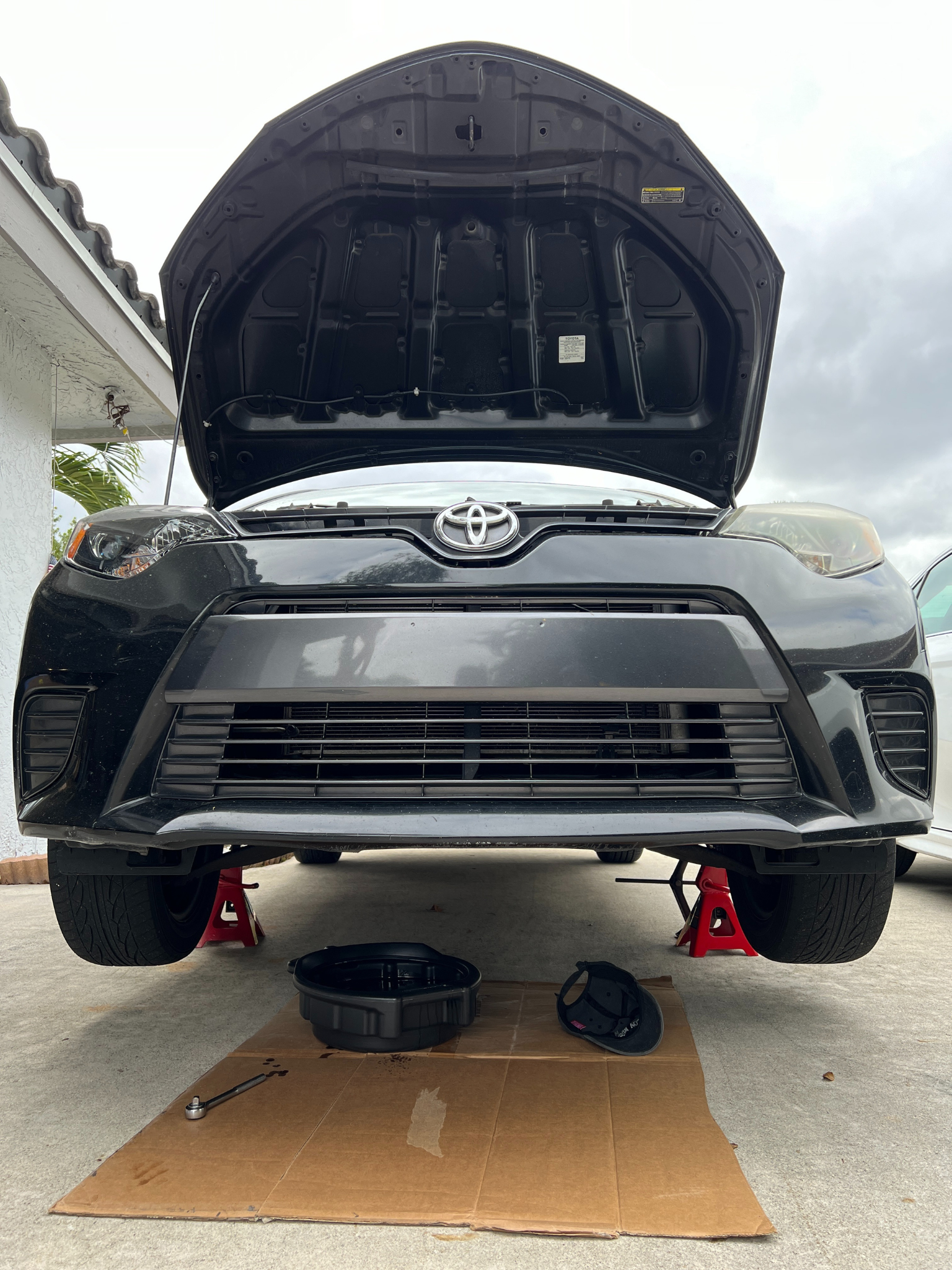 black toyota corolla lifted by two jacks stands. and oil pan is underneath the car.